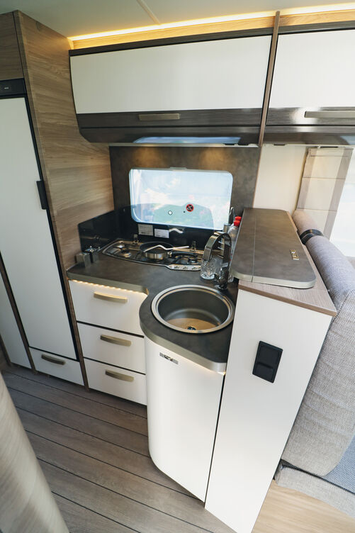 Die auch optisch ansprechende Küche glänzt mit viel Stauraum sowie Dreiflammherd mit elektrischer Zündung, Gussrost und Glasabdeckung und tiefer Edelstahl-Rundspüle mit Haushalts-Mischarmatur.